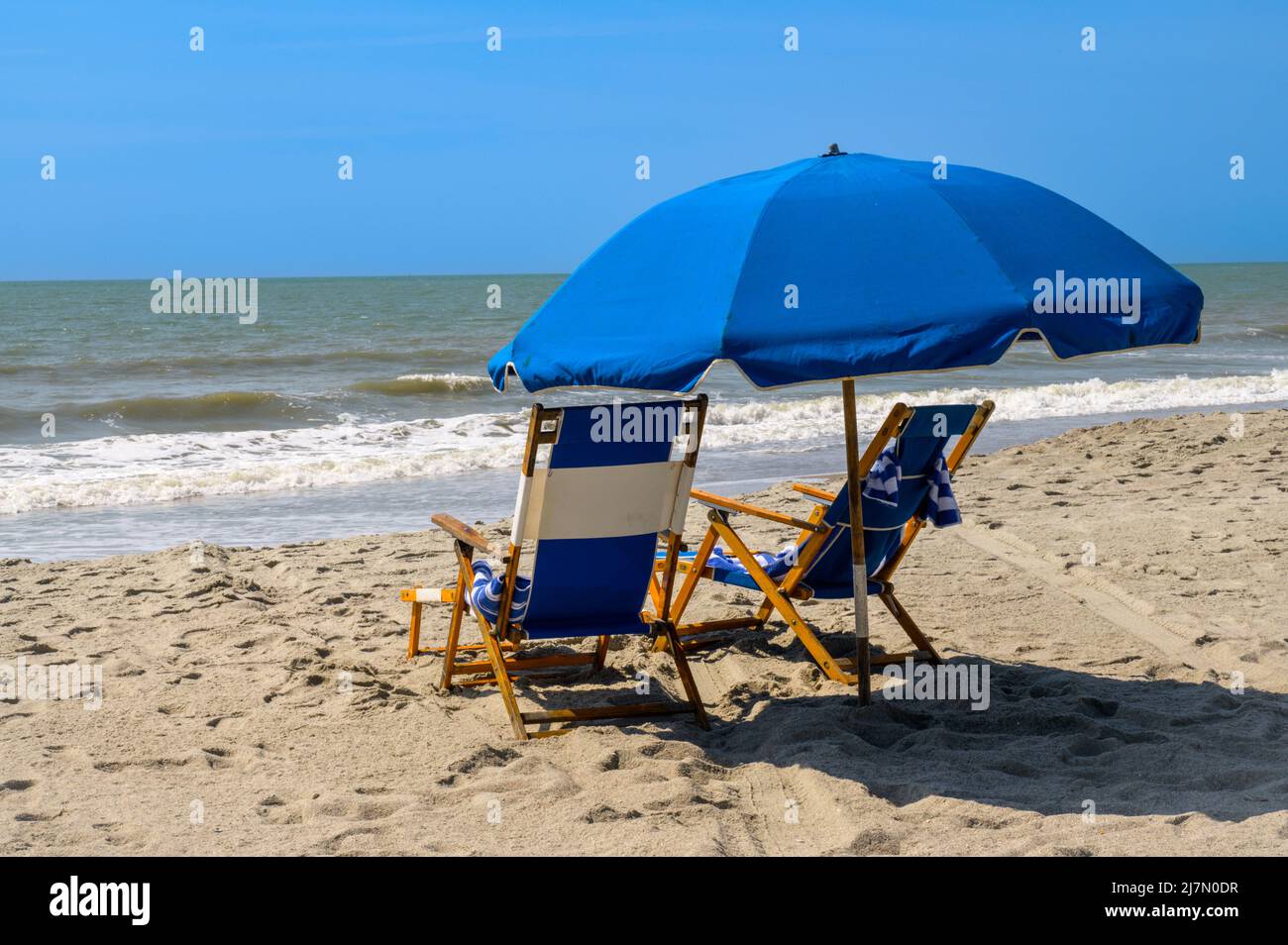 Blue Beach chaises et parasol à l'océan Atlantique lors d'une journée ensoleillée avec des vagues qui s'écrasant sur la plage. Le sable est brun et brun. Les chaises sont bleues Banque D'Images