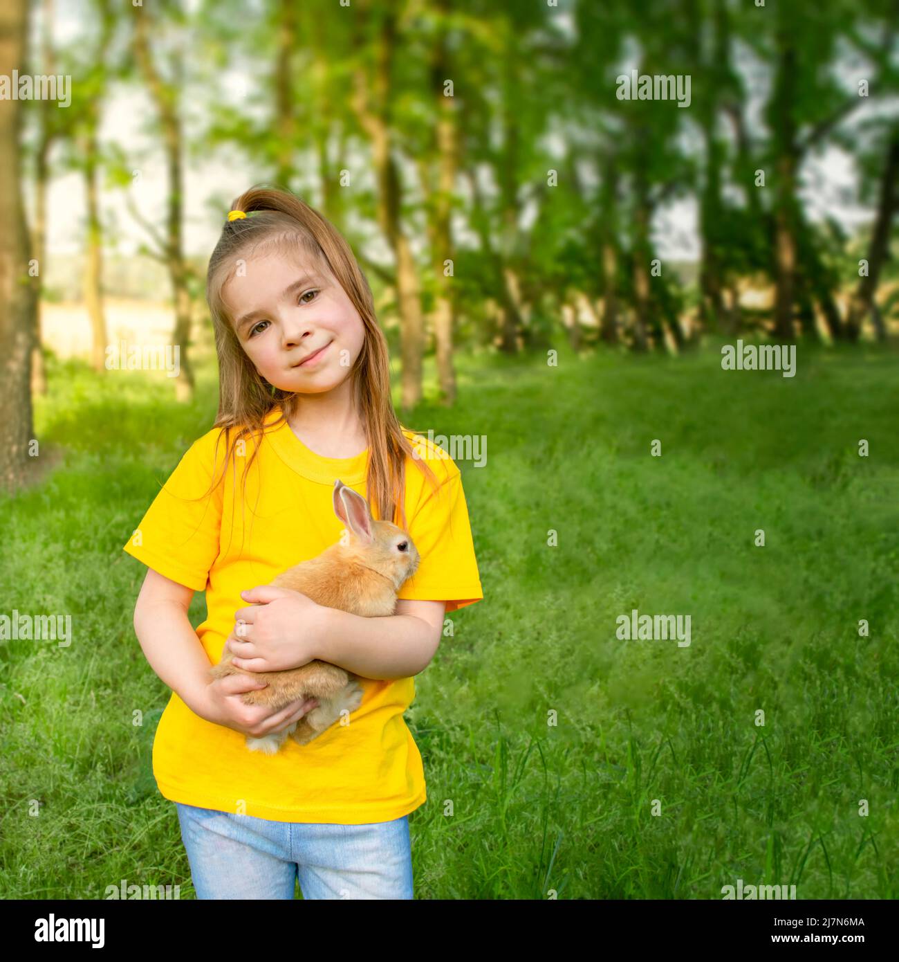 La fille tient un vrai lapin contre le fond de plantes vertes au soleil. Activités de plein air pour les enfants avec animaux de compagnie. Banque D'Images