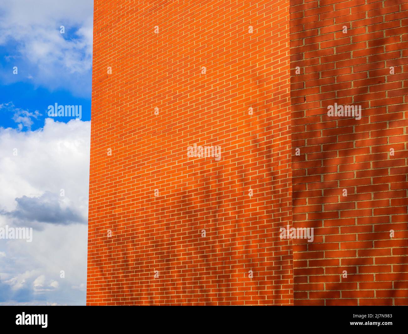 Mur d'un bâtiment en brique rouge avec ciel bleu et nuages en arrière-plan. Banque D'Images