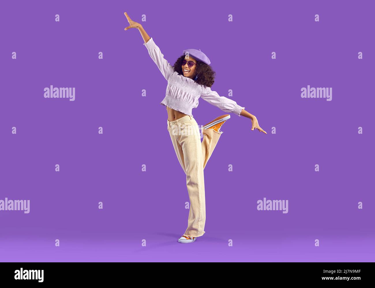 Happy Black Girl dans une tenue décontractée debout sur un pied sur fond violet studio Banque D'Images
