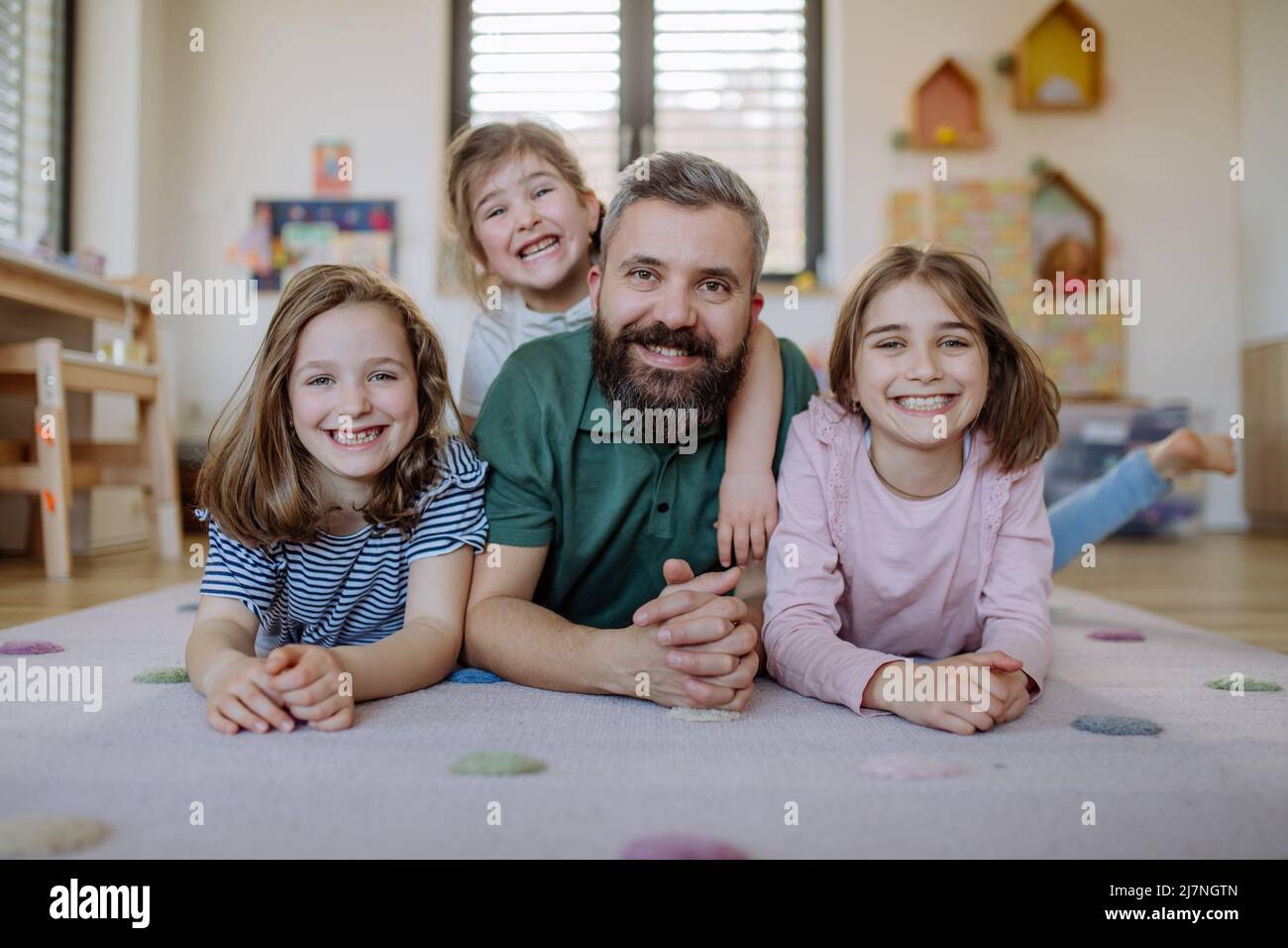 Père joyeux avec trois petites filles jouant ensemble à la maison. Banque D'Images