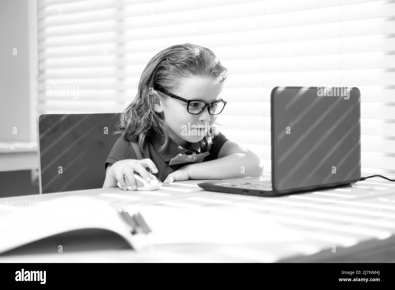 Un jeune garçon qui écrit ses devoirs à l'aide d'un ordinateur portable pour étudier. Petit étudiant, élève apprenant en ligne. Banque D'Images