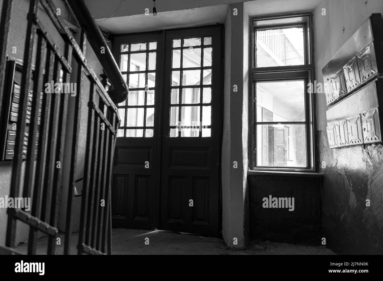 Photo à l'intérieur du couloir d'un ancien immeuble d'appartements, le soleil brille à travers les fenêtres et la porte d'entrée, peinture brune ancienne et sol en pierre. Noir et Banque D'Images