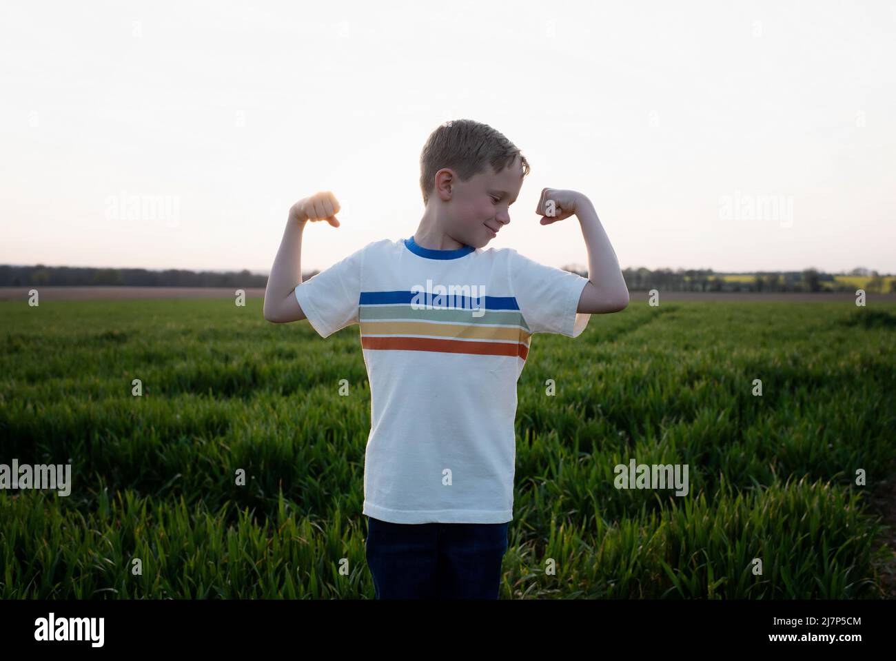 l'enfant fléchit ses muscles pendant qu'il joue à l'extérieur au coucher du soleil Banque D'Images