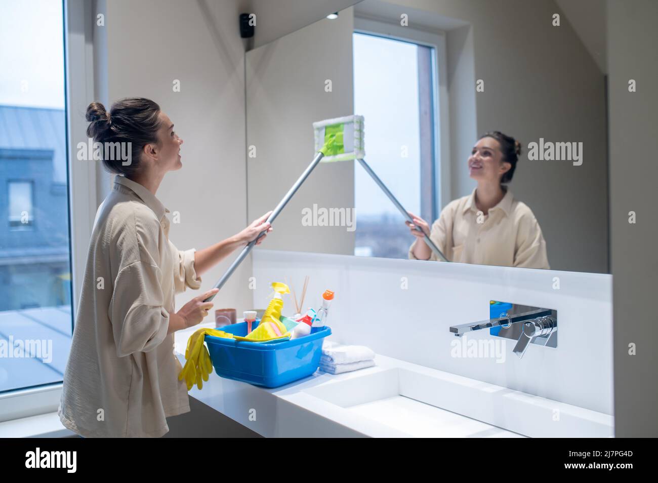 Une jeune femme nettoie le miroir dans la salle de bains Banque D'Images