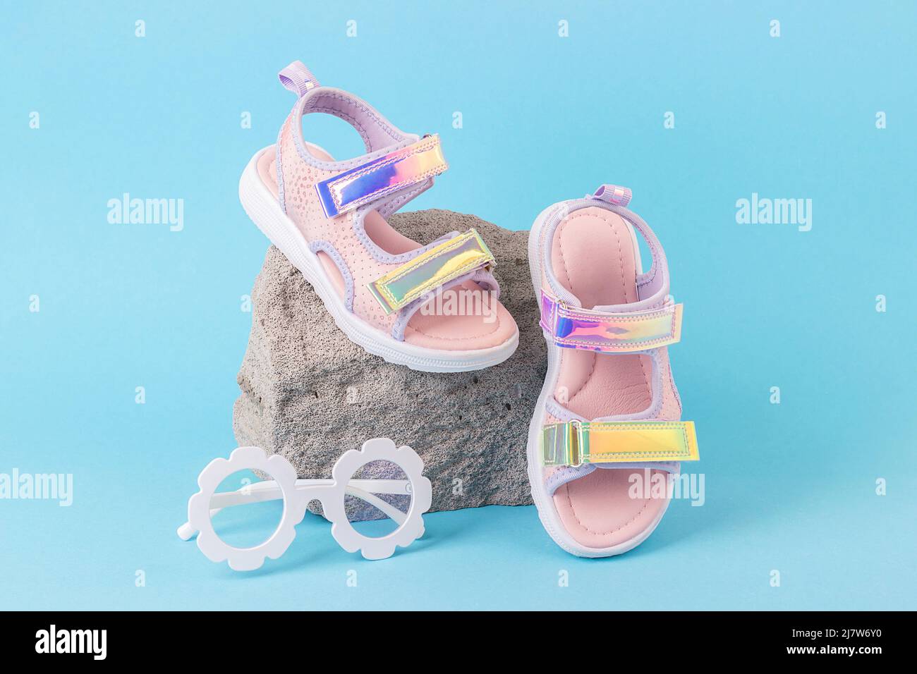 Sandales holographiques élégantes pour enfants et lunettes de soleil sur fond bleu et pierre grise. Chaussures d'été à la mode. Vue avant. Banque D'Images