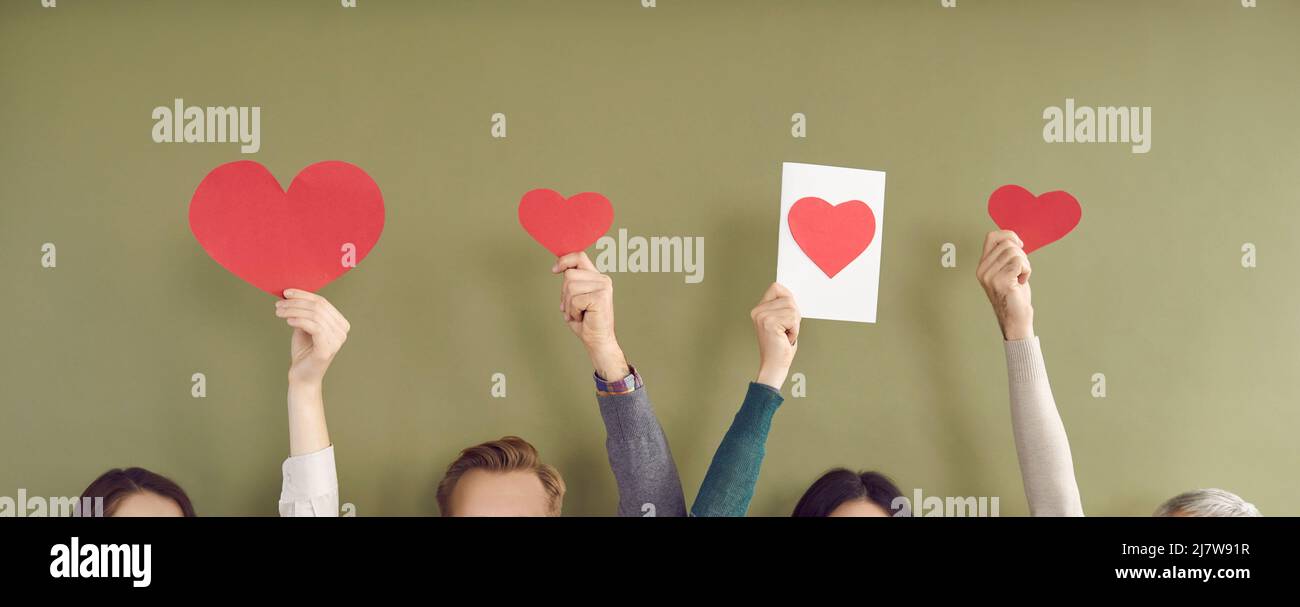 Papier rouge coeurs de différentes tailles dans les mains de personnes méconnaissables sur fond kaki. Banque D'Images