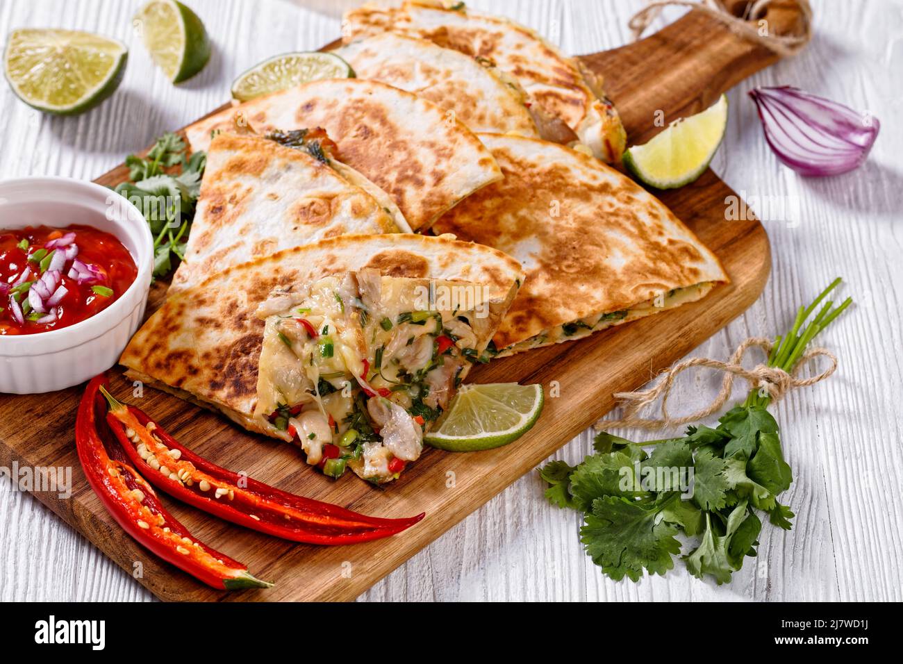 gros plan de quesadilla mexicaine avec poulet, oignon vert, fromage, piment, coriandre servie avec de la sauce tomate et de la lime sur une planche à découper en bois Banque D'Images
