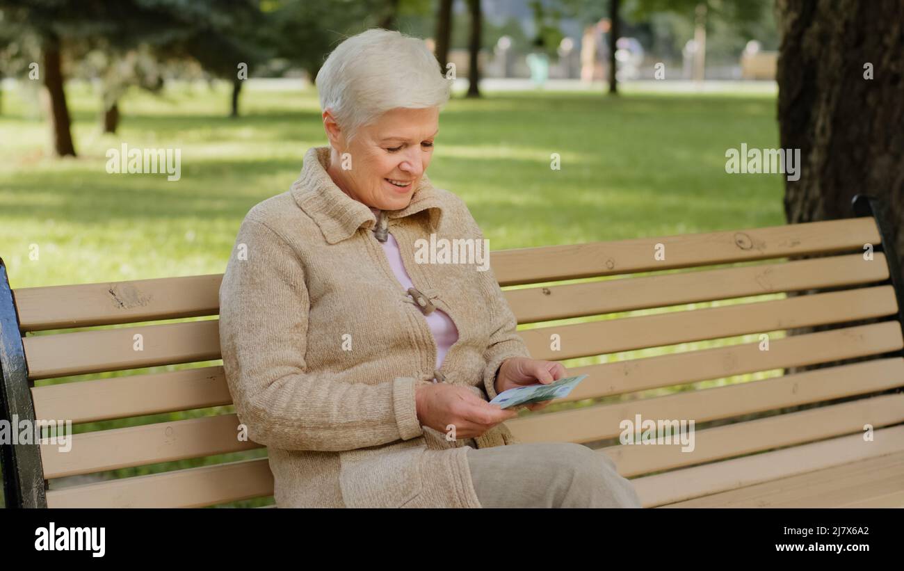 Souriant gris-cheveux succès caucasienne femme mature avec pile de l'euro dans les mains en extérieur. La femme pensionnée vérifie le montant de l'argent comptant Banque D'Images