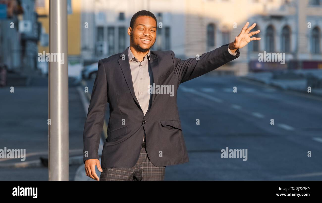 Homme d'affaires ou directeur moderne qui fait la gestuelle pour donner un signal au chauffeur de voiture dans la rue dans la grande ville. Concept de service de taxi. Attrayant Afro-américain Banque D'Images