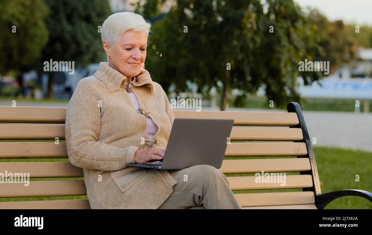 Belle femme âgée heureuse utilisant un ordinateur portable en plein air femme d'affaires d'âge moyen dactylographiant sur le clavier et souriant, dame âgée naviguant sur Internet ou Banque D'Images