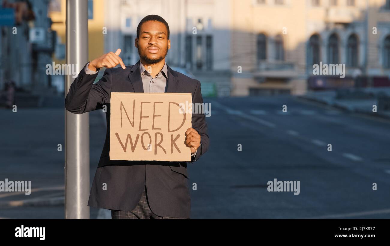 L'homme d'affaires de course mixte tenant l'enseigne a besoin de l'index des points de travail. Portrait d'un jeune homme debout sur une affiche de garde extérieure. Blanc millénaire tiré Banque D'Images