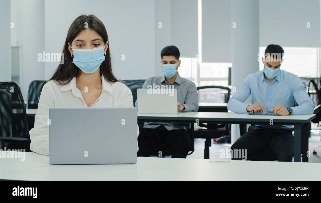 Le personnel multiethnique s'assoit dans un espace de travail avec ordinateurs portables pendant la journée de travail dans un bureau moderne. Petite fille pensive occupée avec la tâche de travail. Portez des masques pour le visage, gardez-les Banque D'Images