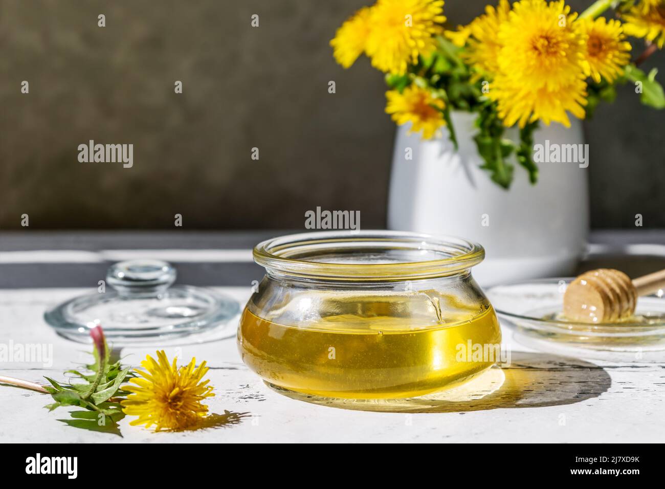 Miel de pissenlit dans un pot sur la table en bois blanc avec fleurs et cuillère à broche de miel sur un plateau en verre Banque D'Images