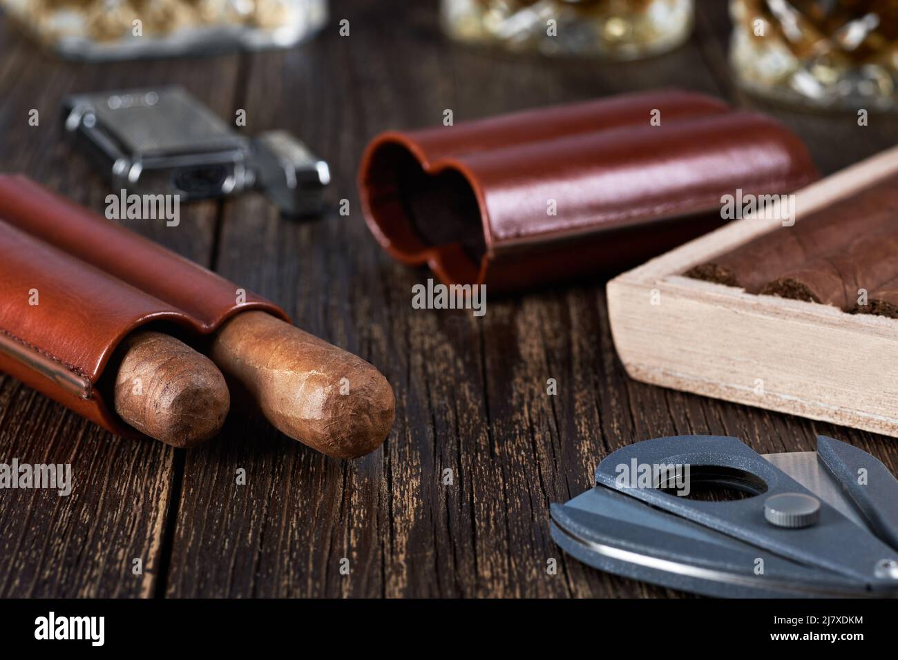 Deux cigares cubains dans un étui en cuir avec une boîte en bois sur une table brune ancienne. Verre de whisky sur un arrière-plan flou. Banque D'Images