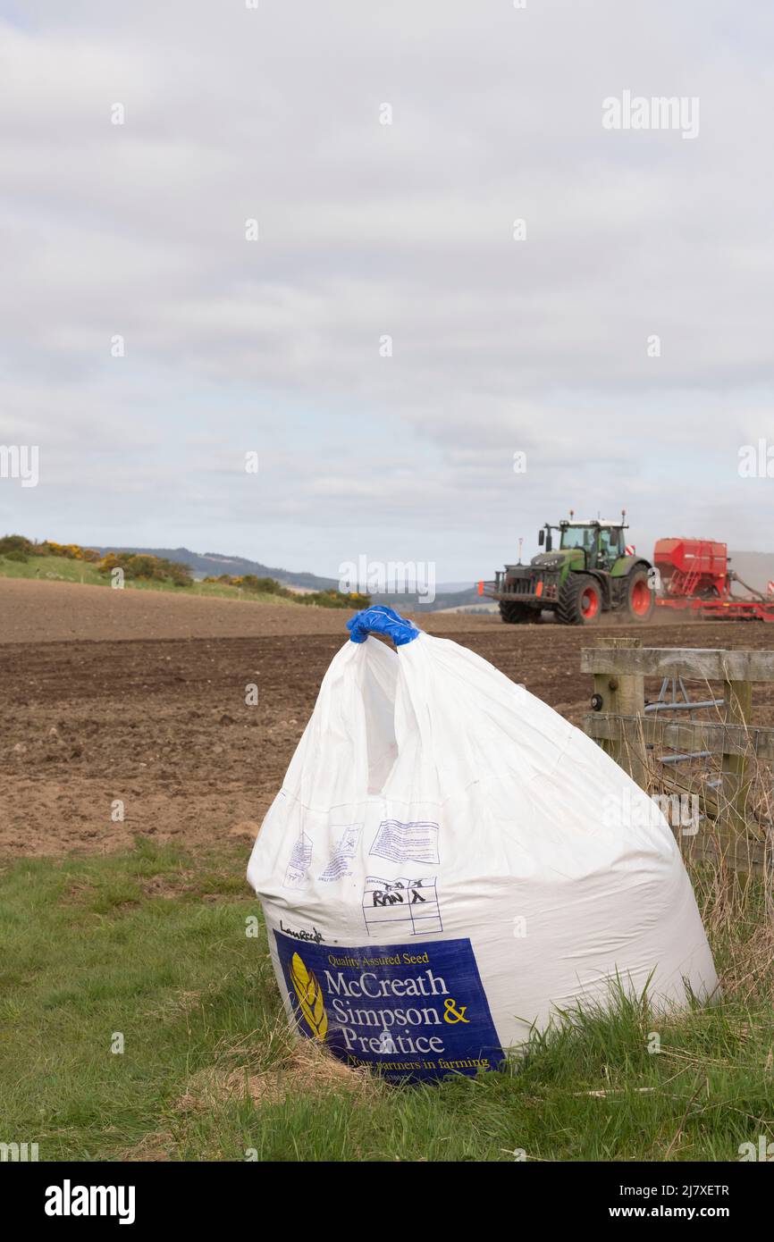 Un sac de semences d'orge à une porte d'entrée au printemps, avec un tracteur vert tractant un semoir fonctionnant en arrière-plan Banque D'Images