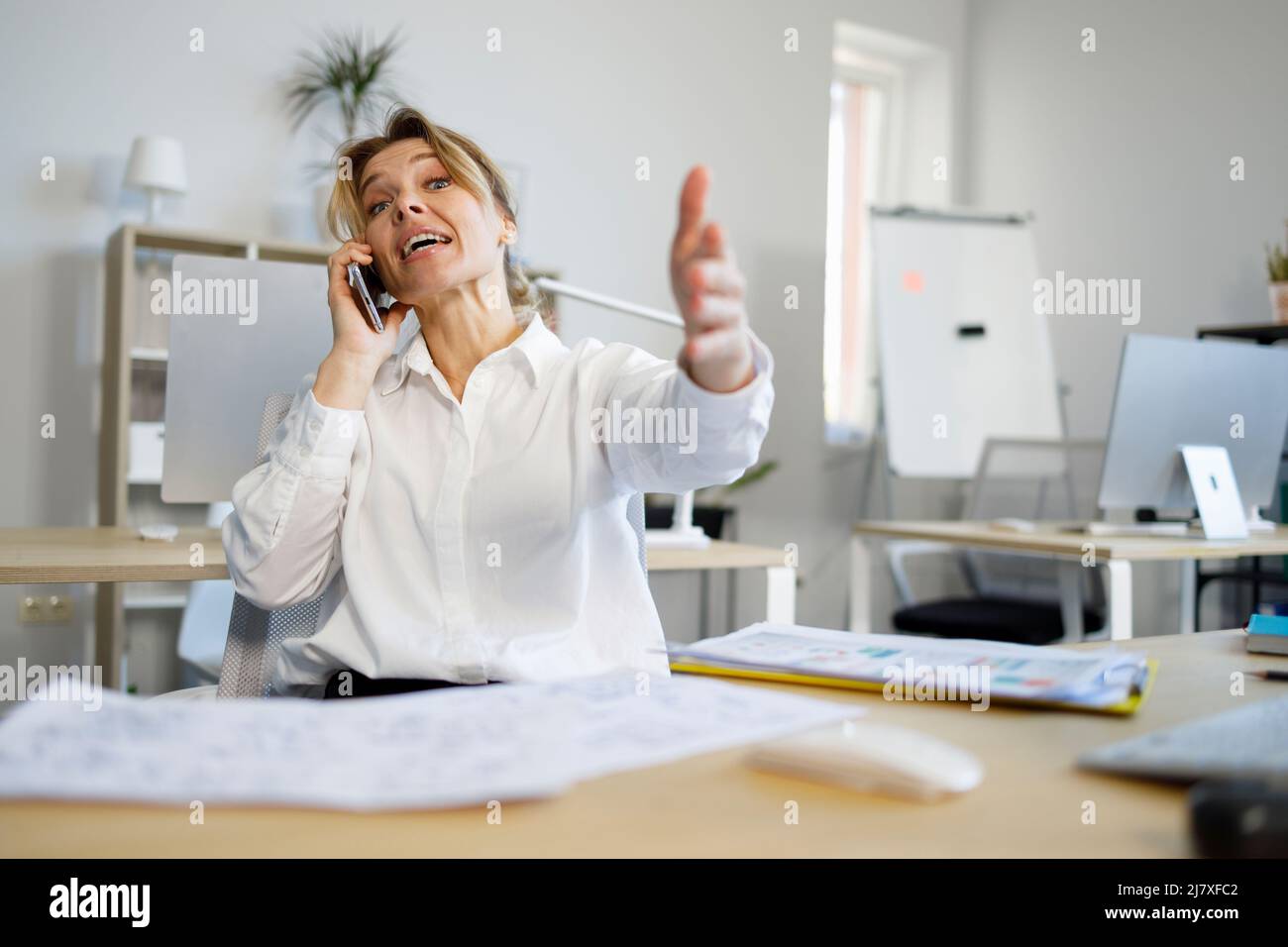 Femme d'affaires émotive parlant au téléphone et pointant avec sa main à la caméra Banque D'Images