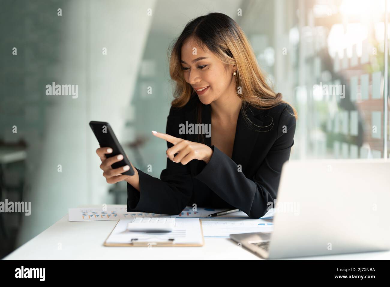 Femme d'affaires asiatique agitant les poings, a obtenu de bonnes nouvelles sur le téléphone mobile intelligent dans le bureau, le réseau social, les appels vidéo, la communication. Banque D'Images