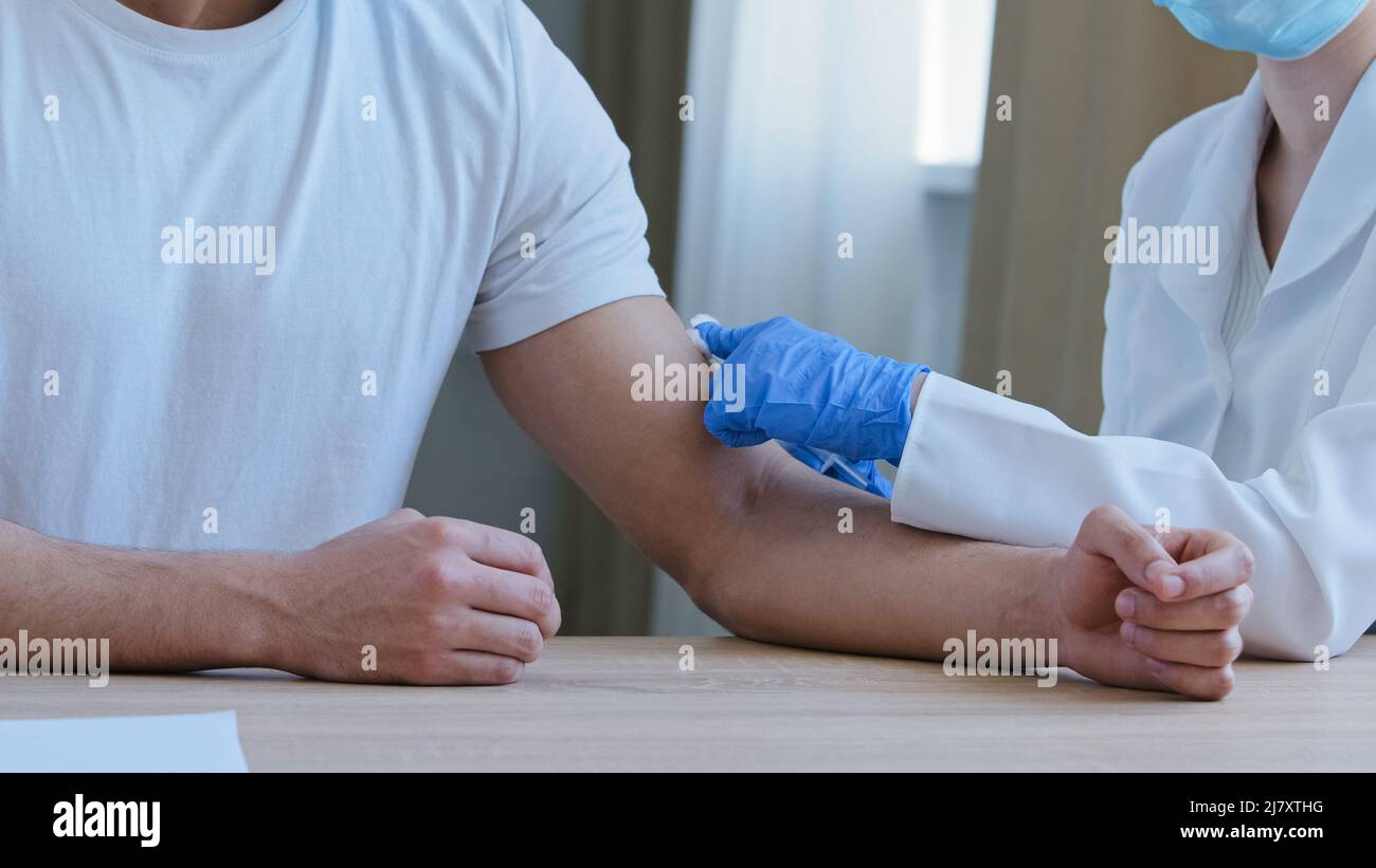 Gros plan non reconnaissable infirmière médecin dans un manteau médical et gants en latex donnant l'injection dans l'épaule à un patient d'homme arabe dans la vaccination de t-shirt blanc dans Banque D'Images