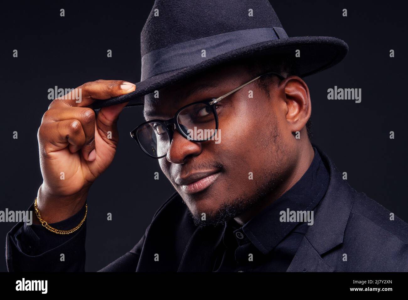 jeune beau afro-américain mélancolie garçon dans une veste et des lunettes sur un fond noir dans le studio.mystère et chagrin se cachent Banque D'Images