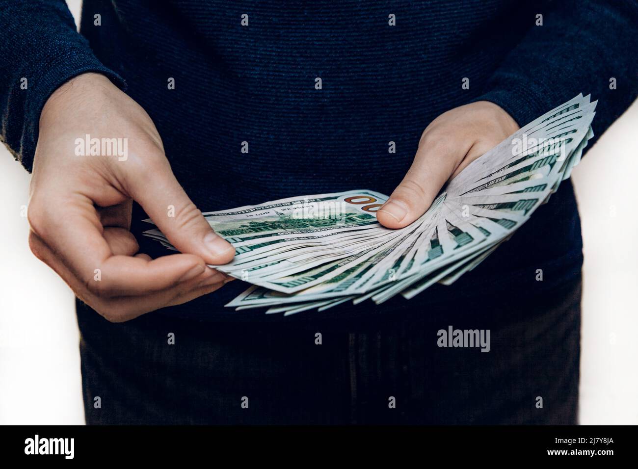 Un homme tient un fan de 100 billets de dollars dans ses mains et les compte. Banque D'Images