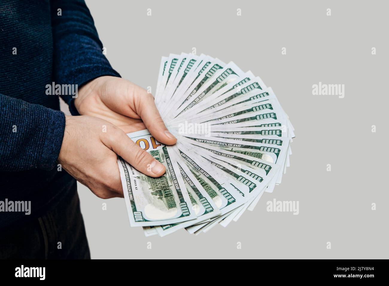 Un homme tient un fan de 100 billets de dollars dans ses mains sur fond clair Banque D'Images