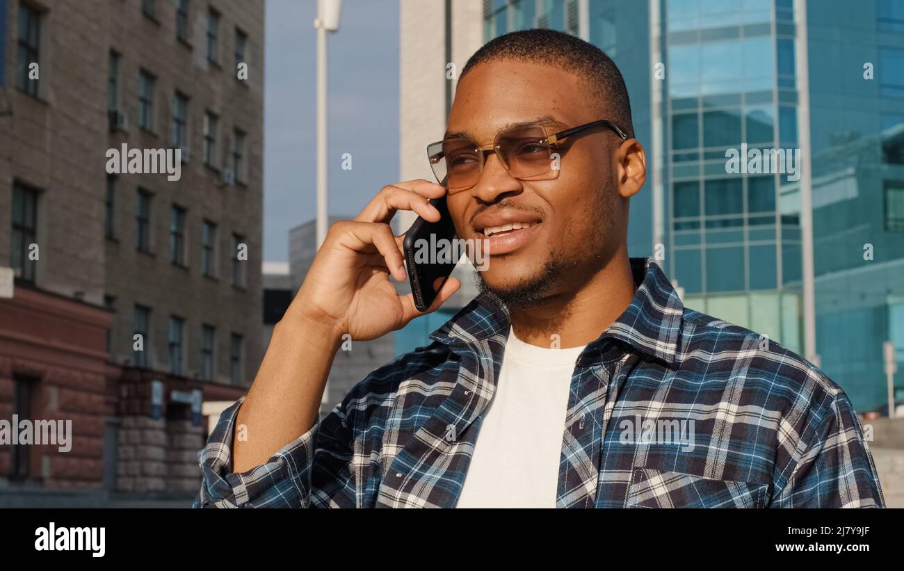 Élégant homme africain heureux portant des lunettes de soleil tendance parle téléphone mobile en ville. Smartphone à visage parlé à la peau foncée pour homme en gros plan. Portrait de Banque D'Images