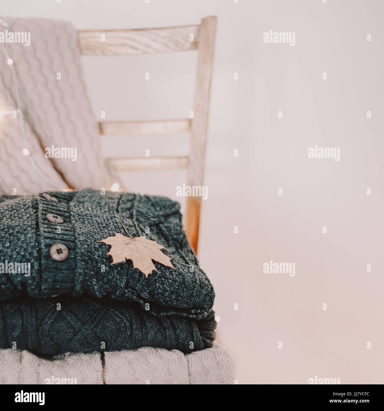 une pile de chandails en laine chaude et une feuille d'érable sur une chaise, concept d'automne Banque D'Images