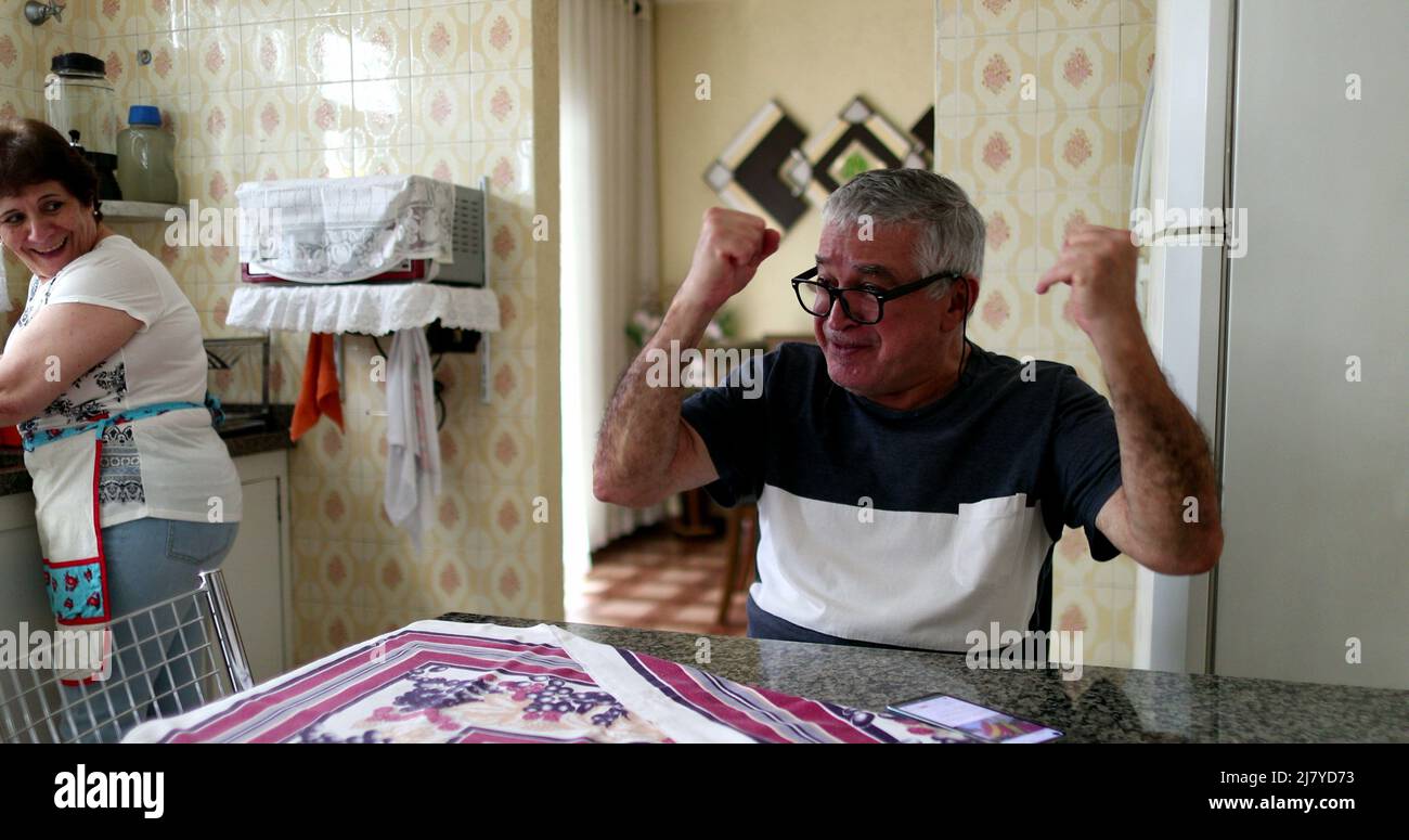 Joyeux senior commémorant les bonnes nouvelles sur le téléphone portable. Couple marié à la cuisine maison célébrant Banque D'Images