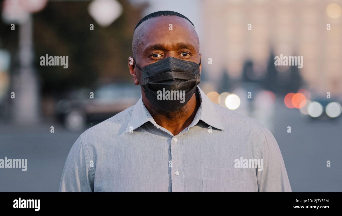 Adulte adulte mature africain américain homme portant un masque médical de protection noir posant à l'extérieur. Homme d'affaires âgé debout dans la rue pendant une pandémie Banque D'Images