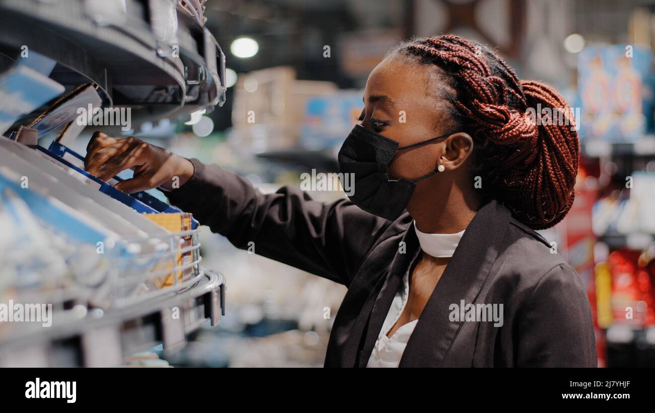 Gros plan vue du côté afro-américain fille dans le masque médical jeune femme femelle consommateur shopper stands dans le magasin de supermarché choisir des biens d'achat Banque D'Images