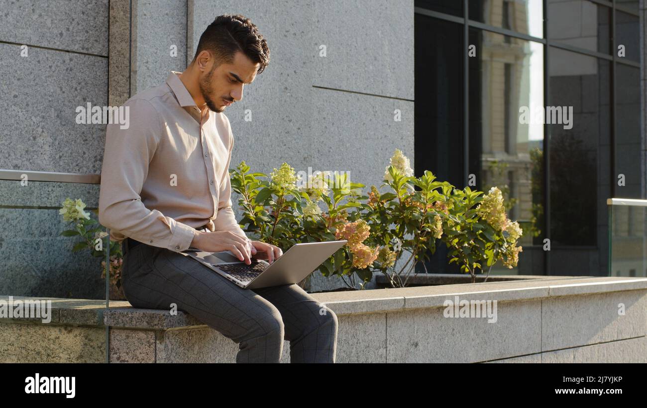 Jeune homme d'affaires formel utilisateur Manager travailleur étudiant assis sur la terrasse près du bureau de l'entreprise immeuble dans la rue à l'extérieur avec ordinateur portable étudiant Banque D'Images