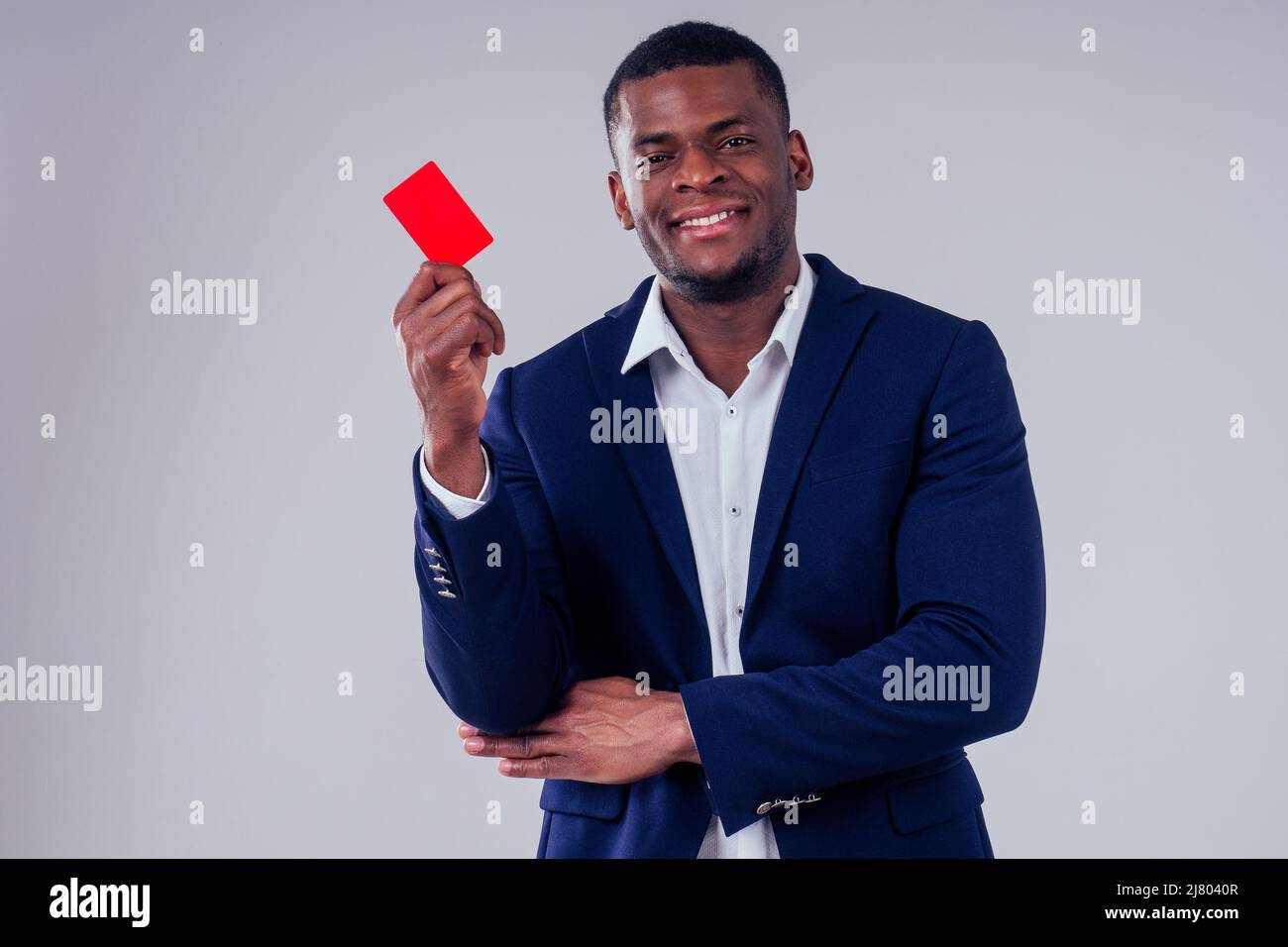 élégant afro-américain en costume noir pantalon et veste avec un grand col de chemise tenant la carte de crédit rouge en plastique dans le studio sur fond blanc Banque D'Images