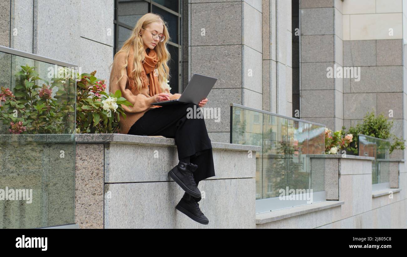 Femme d'affaires confiante travaillant à l'extérieur jeune fille caise réussie assise près d'un bâtiment de bureau dactylographiant sur ordinateur portable dans l'application femelle utilisant le sans fil Banque D'Images