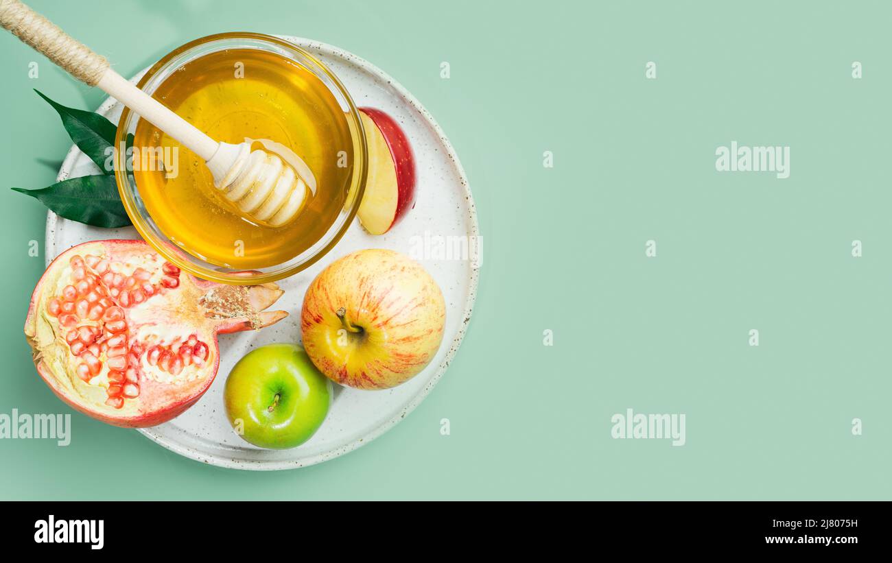 Miel, pomme et grenade sur fond vert menthe. Concept juif nouvel an Joyeux vacances Rosh Hashanah. Mise en page créative des symboles traditionnels. Banque D'Images