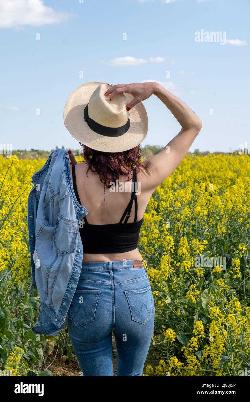 Vue arrière d'une femme debout dans un champ de colza au printemps avec sa main sur la tête, France Banque D'Images