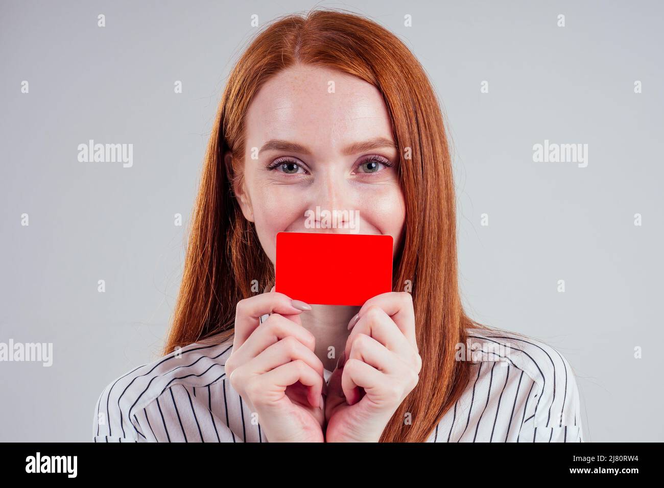 attrayant redhead caucasien femme d'affaires portant une chemise rayée tenant la carte de crédit studio blanc fond noir vendredi vente Banque D'Images