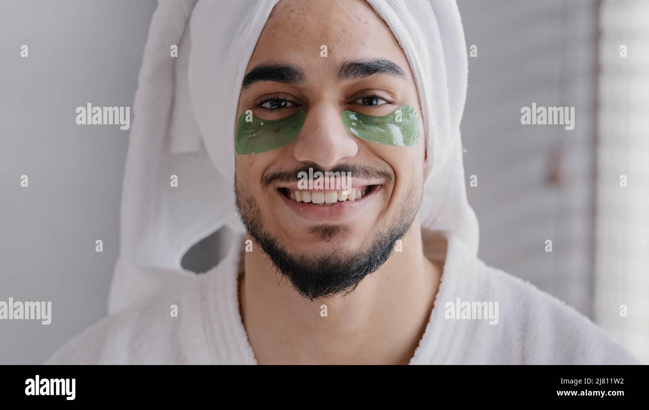 Drôle de portrait homme visage souriant indien arabian homme portant serviette de bain sur la tête colle collant hydrogel yeux-patchs cosmétiques procédures soins de la peau gars Banque D'Images