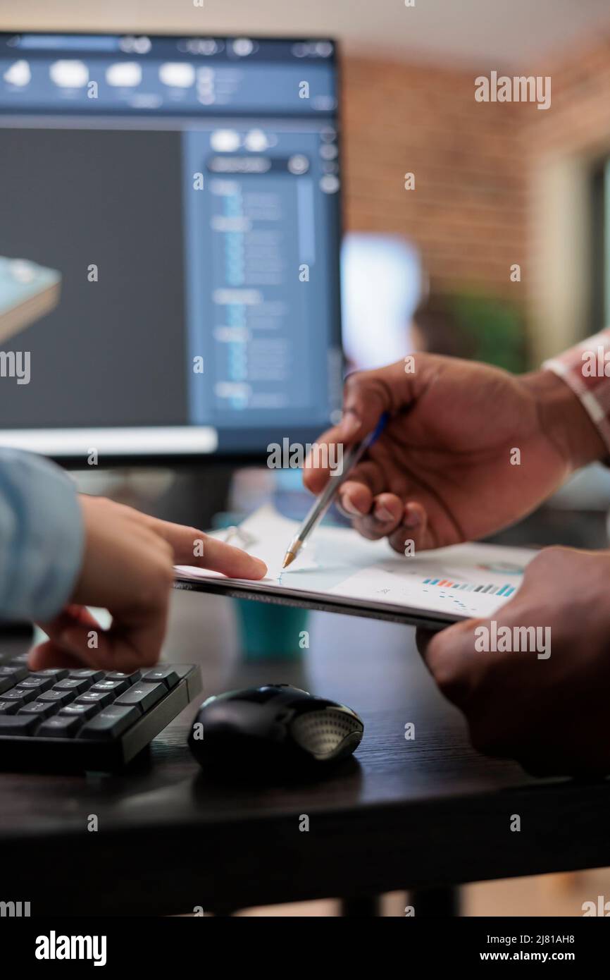 Gros plan de 3D artistes numériques examinant le plan de la scène de croquis et les temps de rendu simulés, les passionnés de l'industrie créative avec la CAO ouvrent en arrière-plan discutant des problèmes techniques tout en pointant vers le presse-papiers Banque D'Images