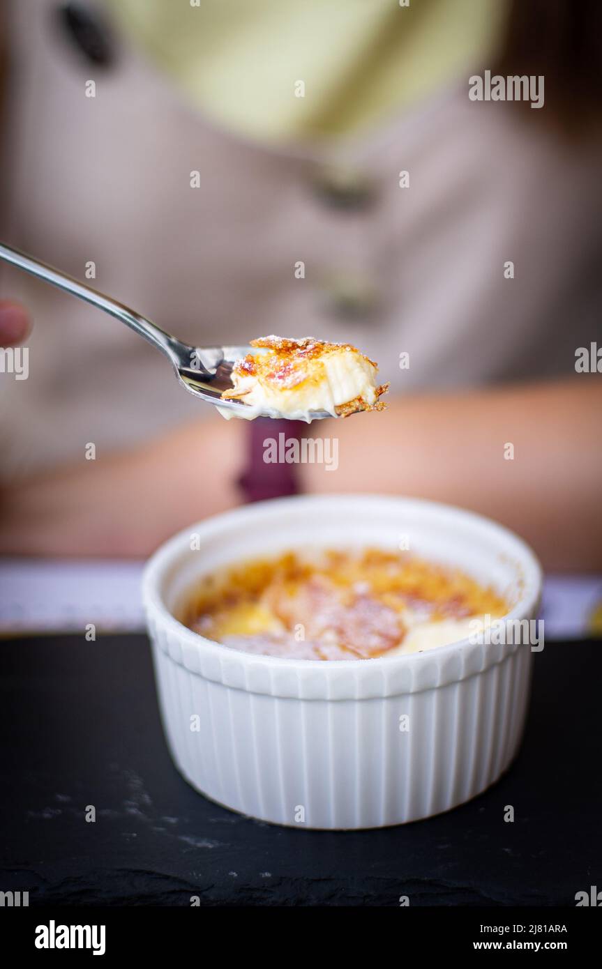 Une jeune femme mangeant une crème brûlée à l'extérieur dans un restaurant, un concept de vacances et de profiter de l'été. Photo verticale. Banque D'Images