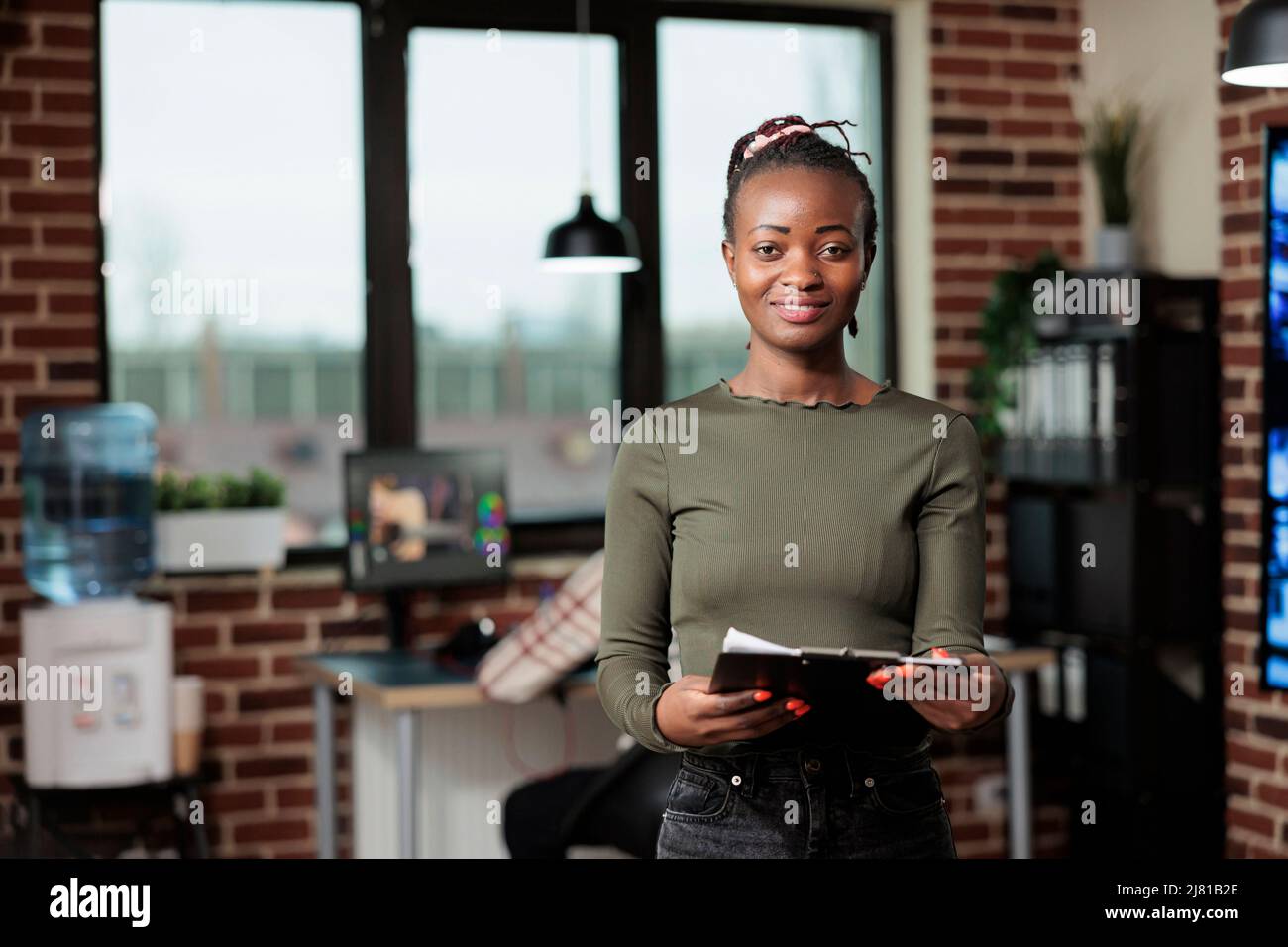 Chef d'équipe du département de production dans le studio d'art numérique. Concepteur artistique plein de confiance dans un espace de travail de bureau avec des documents de presse-papiers tout en souriant à l'appareil photo. Banque D'Images