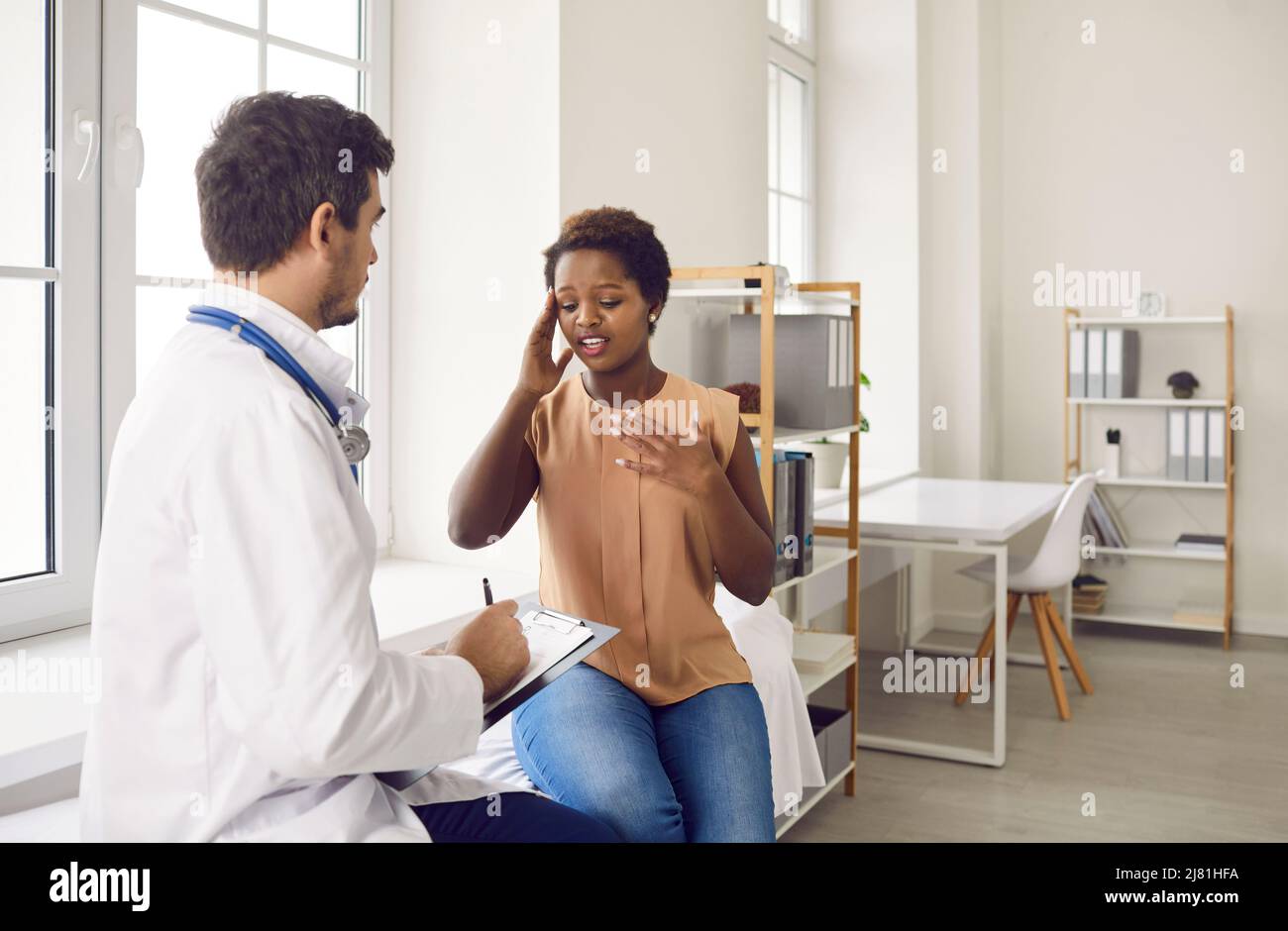 Une jeune femme à la peau sombre gênée parle de maux de tête au médecin lors d'une visite à la clinique. Banque D'Images