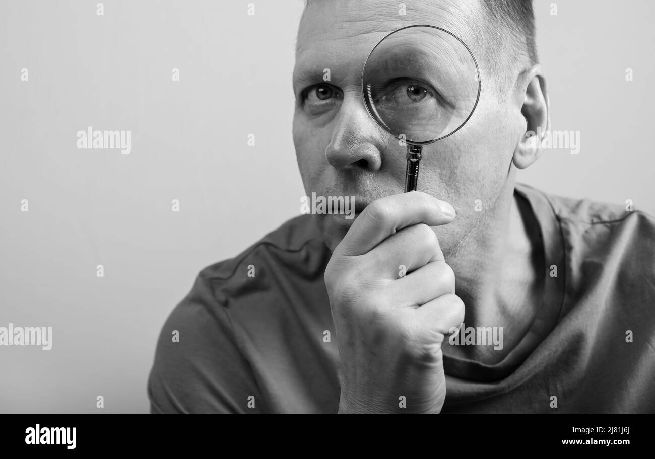 Homme sérieux et mature regardant la loupe. Réalisation de la vérification, recherche d'informations et concept d'analyse. Travail d'espion, comptable, auditeur. Noir et blanc. Photo de haute qualité Banque D'Images