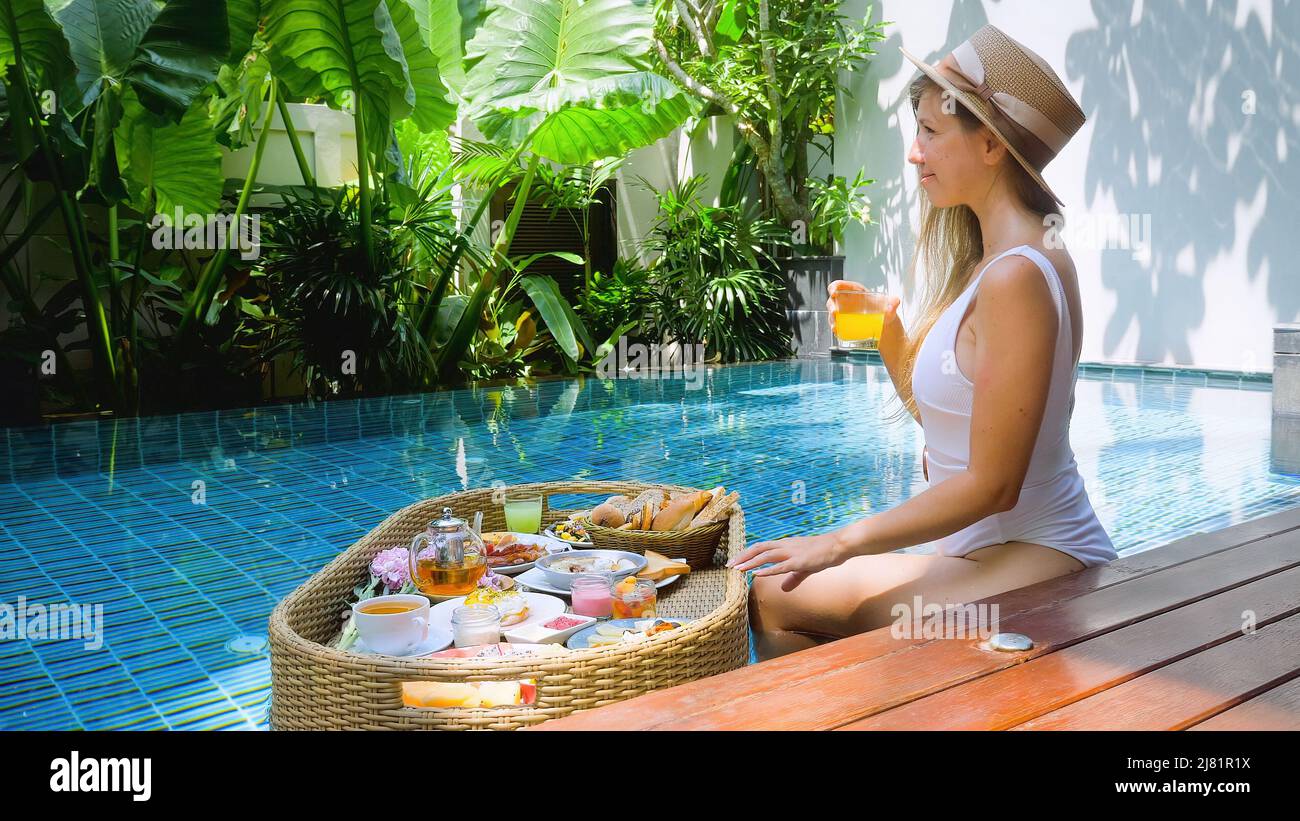 Une jeune femme se détend au bord de la piscine et boit du jus d'orange, une femme sexy en plein air Banque D'Images