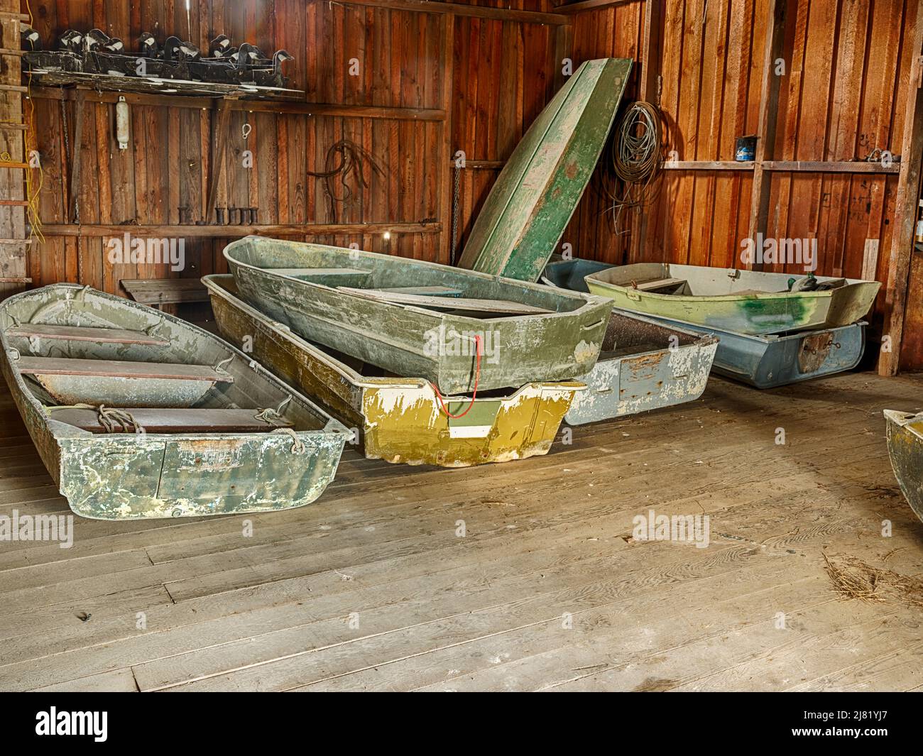 Une petite flotte de petits bateaux est stockée à l'intérieur d'une ancienne hangar à bateaux en bois. Banque D'Images