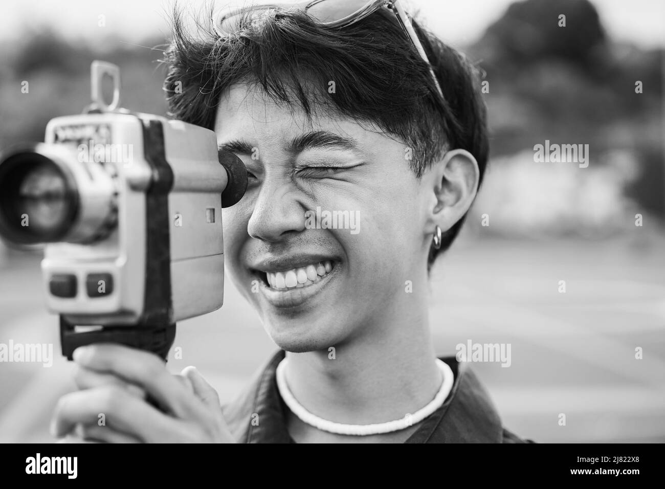 Jeune homme asiatique utilisant une ancienne caméra vidéo d'extérieur - Focus sur l'œil droit - montage en noir et blanc Banque D'Images