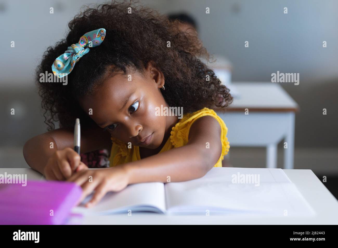 Gros plan d'une écolière afro-américaine de l'élémentaire qui dessine une ligne sur un livre à un bureau en classe Banque D'Images