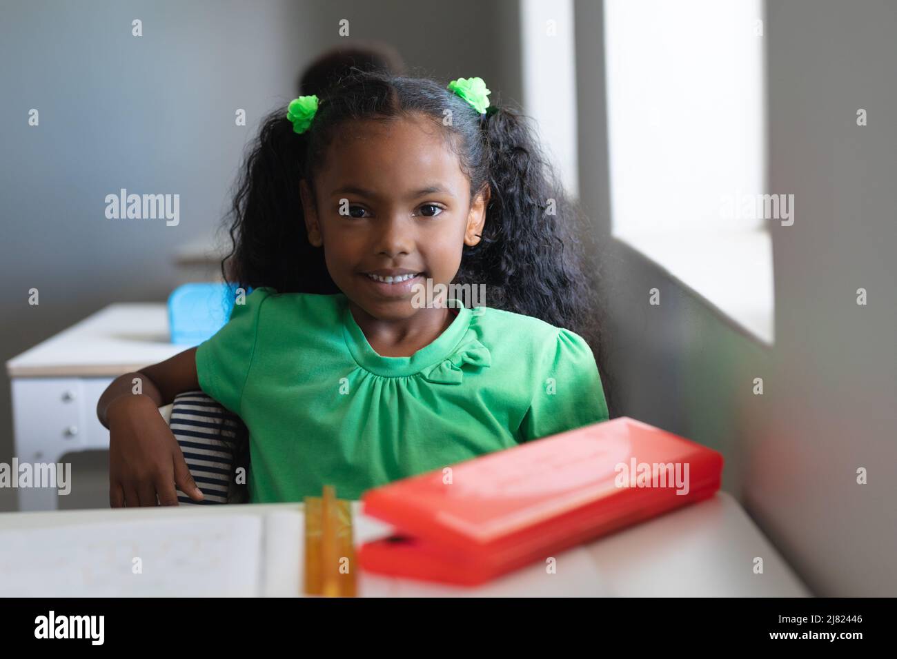 Portrait d'une jeune fille élémentaire afro-américaine souriante et confiante en robe verte, assise au bureau Banque D'Images