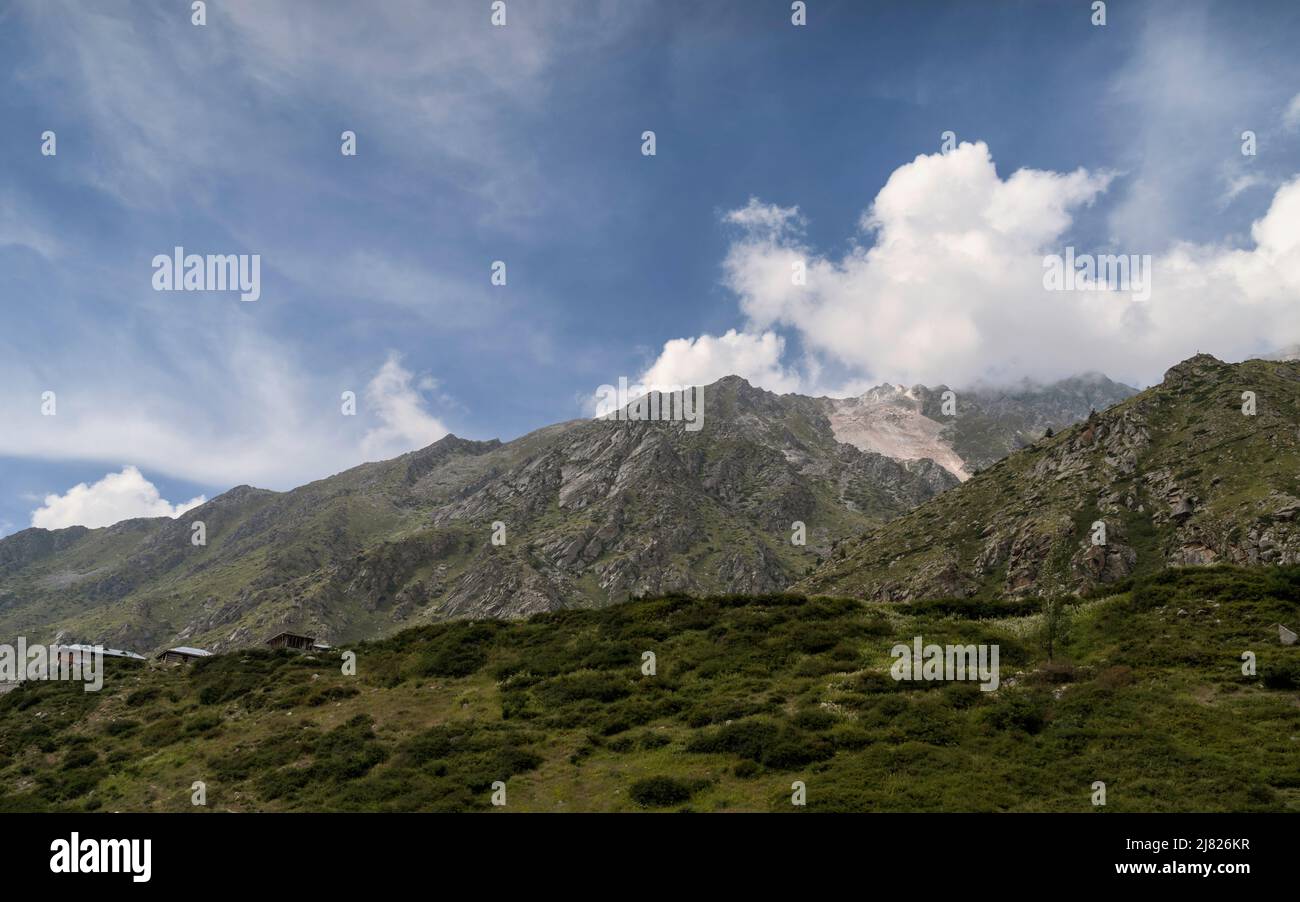 Paysage accidenté avec de faibles formations de flore et flanqué par les pentes et les sommets accidentés des montagnes de l'Himalaya sous le ciel bleu avec des nuages spectaculaires. Banque D'Images
