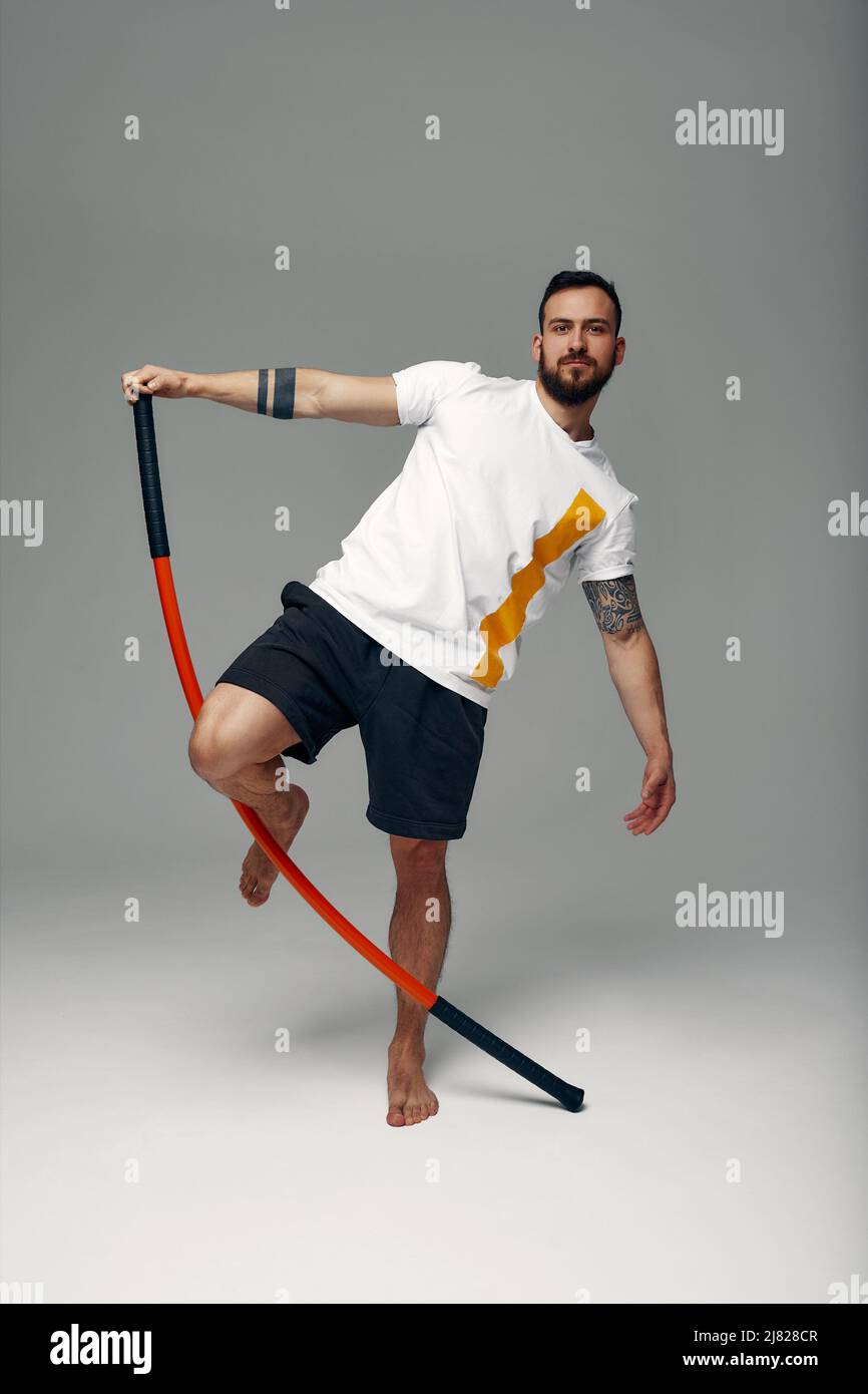 Un combattant en t-shirt blanc et short noir, se tient dans une posture de combat artificiellement et tient un bâton de combat sur fond de studio. Banque D'Images